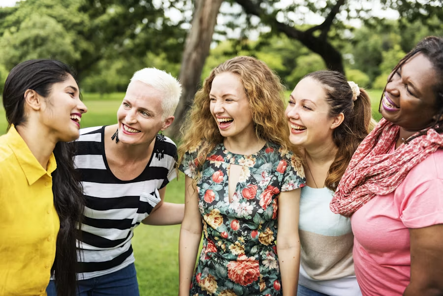 Cinq femmes souriantes de diverses origines réunies ensemble dans un parc