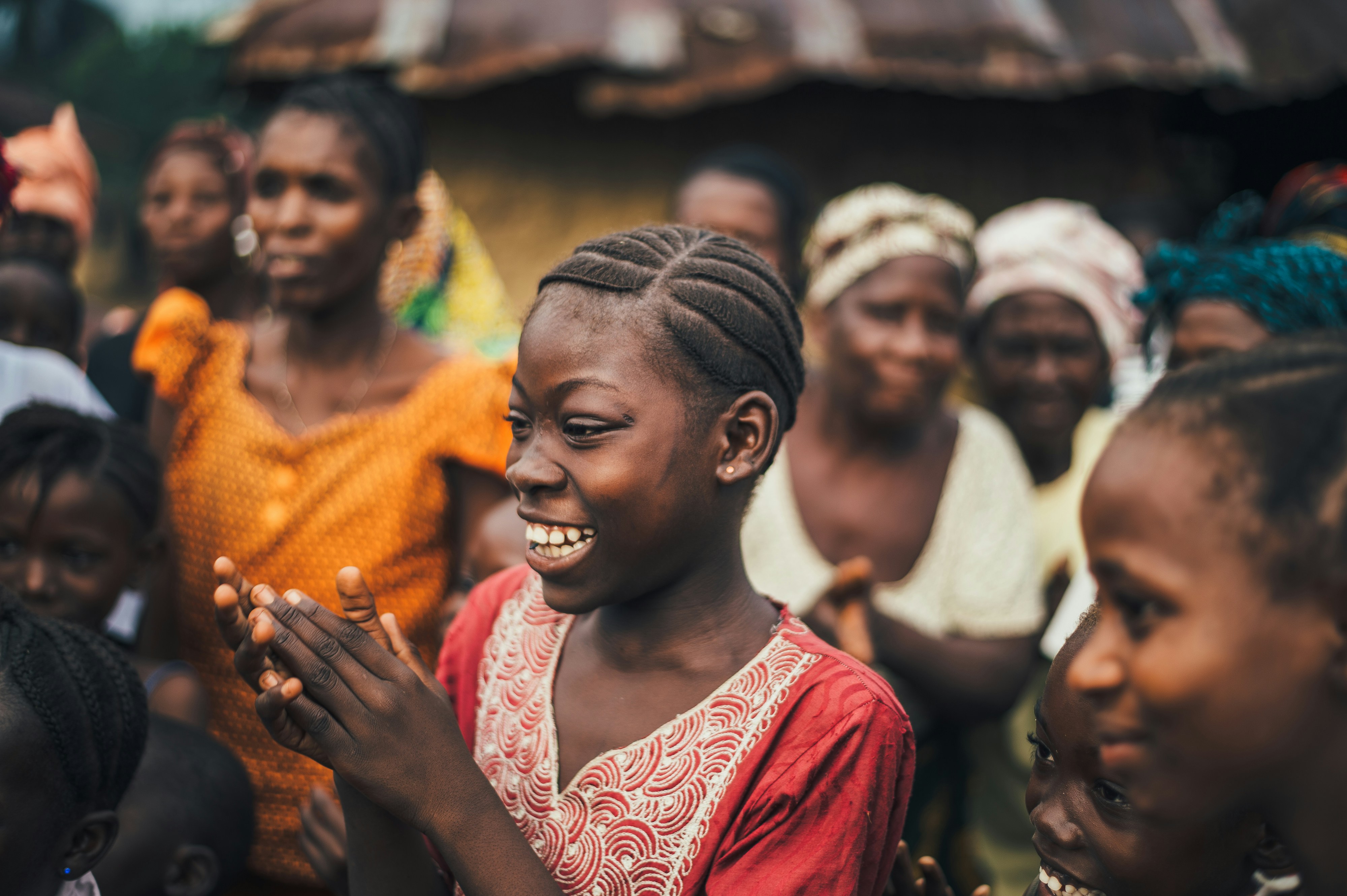 Photographie documentaire authentique et positive, lumineuse et élégante, représentant une communauté composée de femmes et d’enfants en action dans un contexte de solidarité et de développement international. Expressions naturelles, dignité, espoir, entraide et participation communautaire. Composition horizontale large adaptée à une bannière de site web, espace visuel équilibré pour permettre la lisibilité d’un titre en surimpression, palette chaleureuse et naturelle, rendu professionnel, humain et non misérabiliste. Aucun texte ni logo dans l’image.